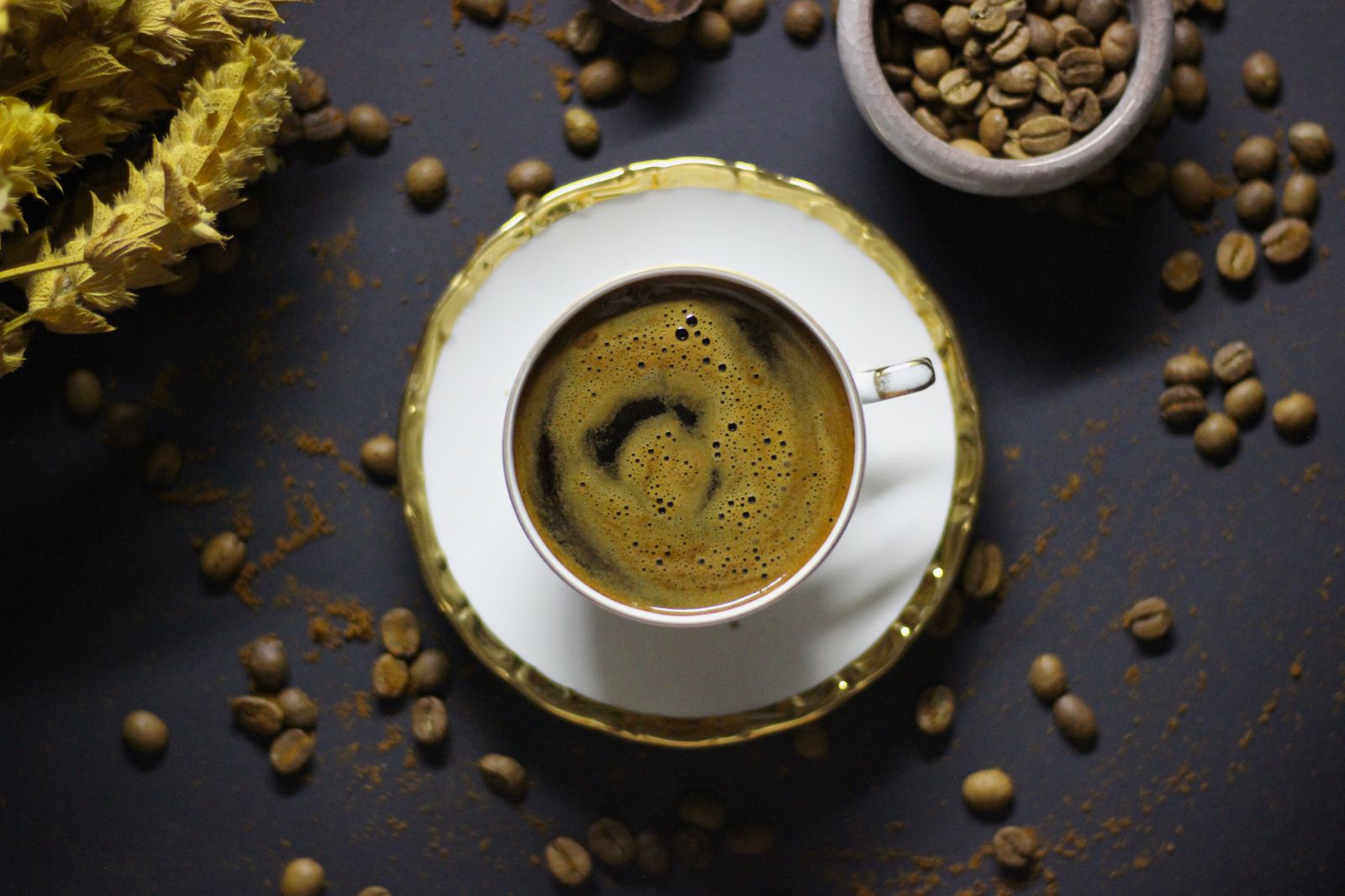 Aerial view of a cup of black coffee surrounded by scattered coffee beans