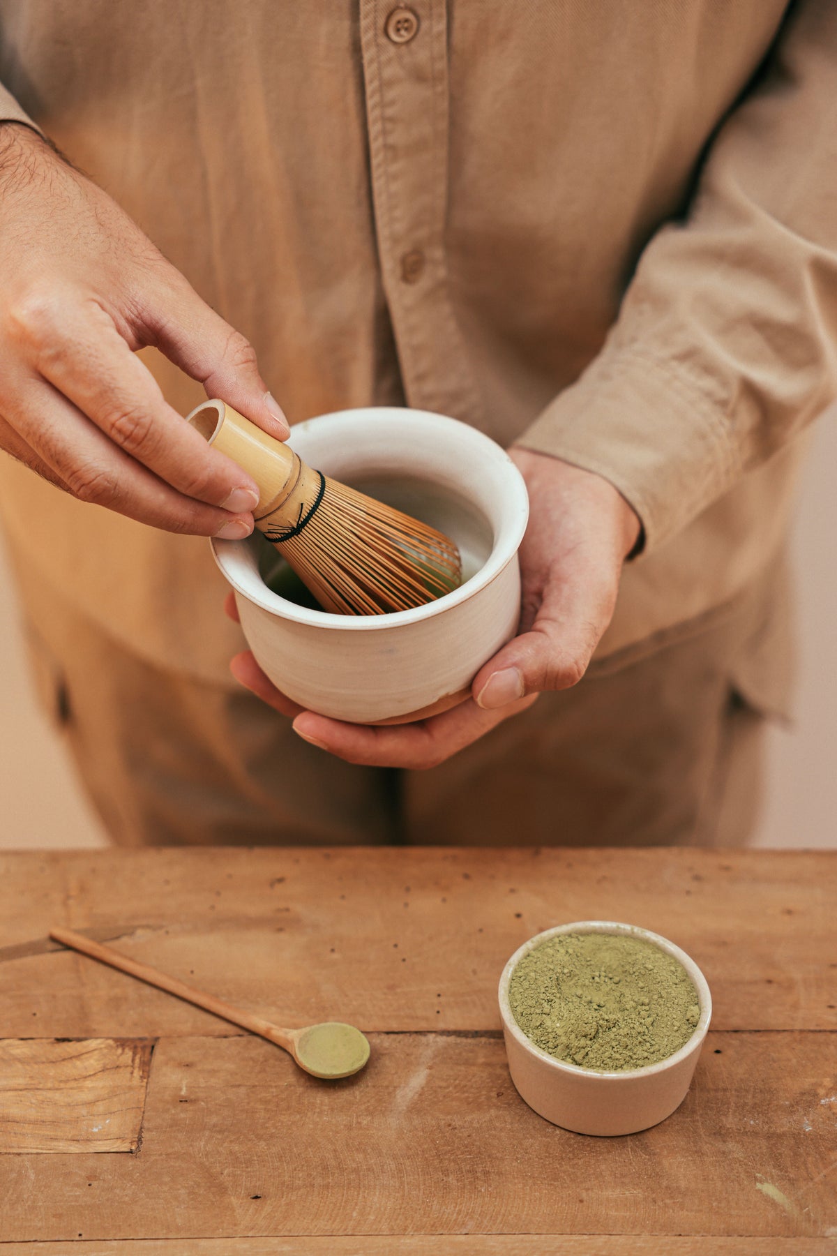 Hands whisking ceremonial matcha in a bowl with a bamboo whisk