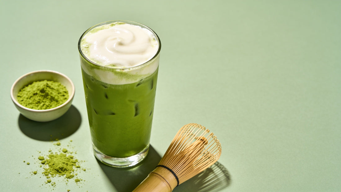 Overhead flat lay of a vibrant iced green matcha latte with matcha powder and a bamboo whisk