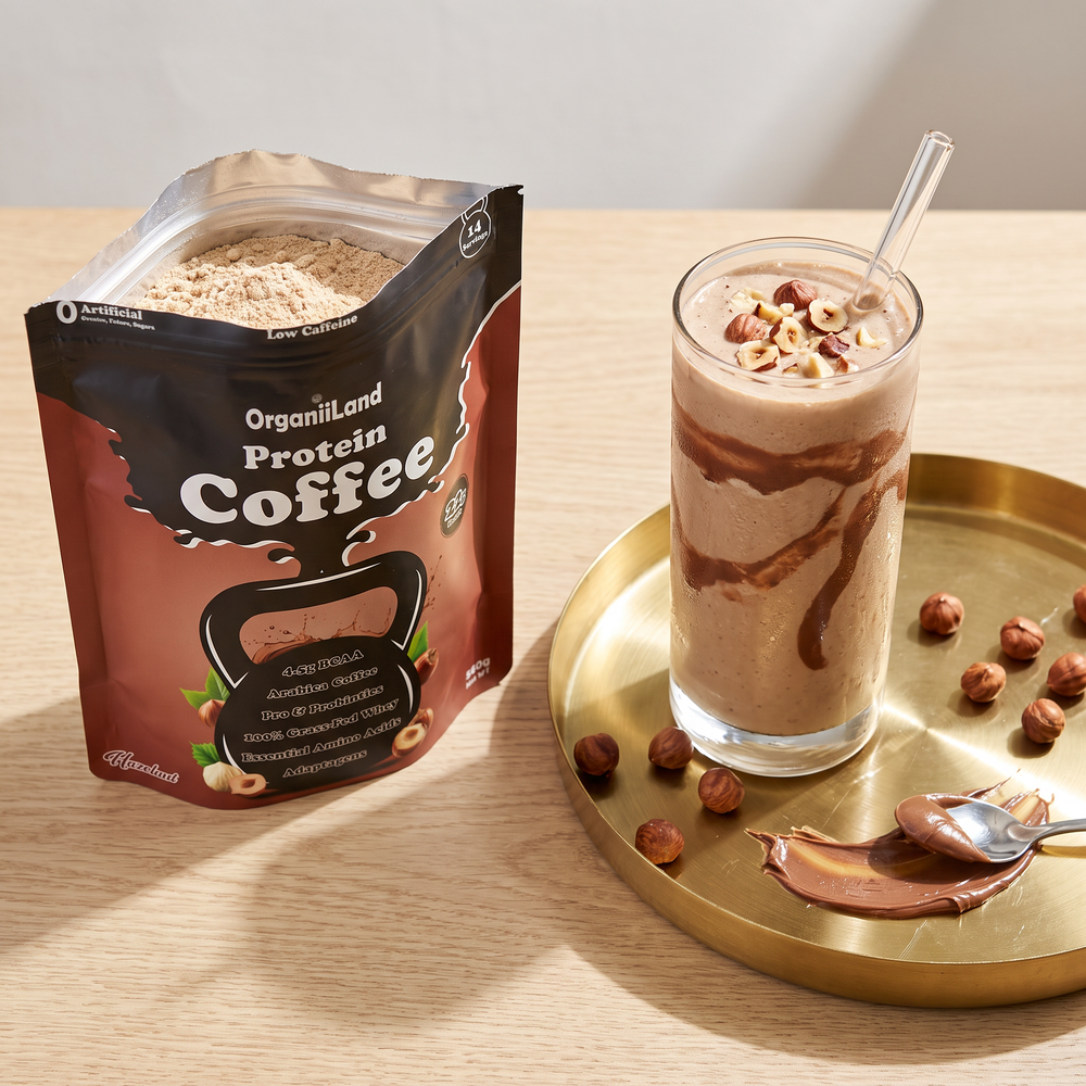 Thick hazelnut protein shake in a glass with a frozen banana and hazelnut butter beside an opened bag of OrganiiLand Hazelnut Protein Coffee