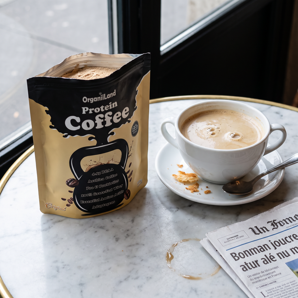 Protein cafe au lait in a wide porcelain bowl-cup on a marble bistro table beside an opened OrganiiLand Original Protein Coffee bag