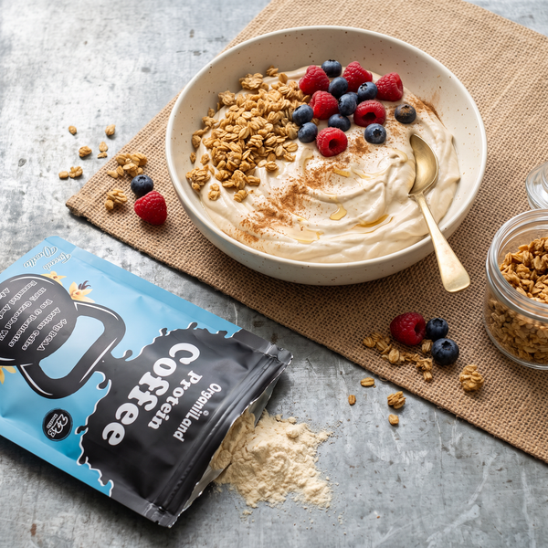 Protein coffee Greek yogurt bowl with granola and berries on a zinc counter beside an opened OrganiiLand French Vanilla Protein Coffee bag