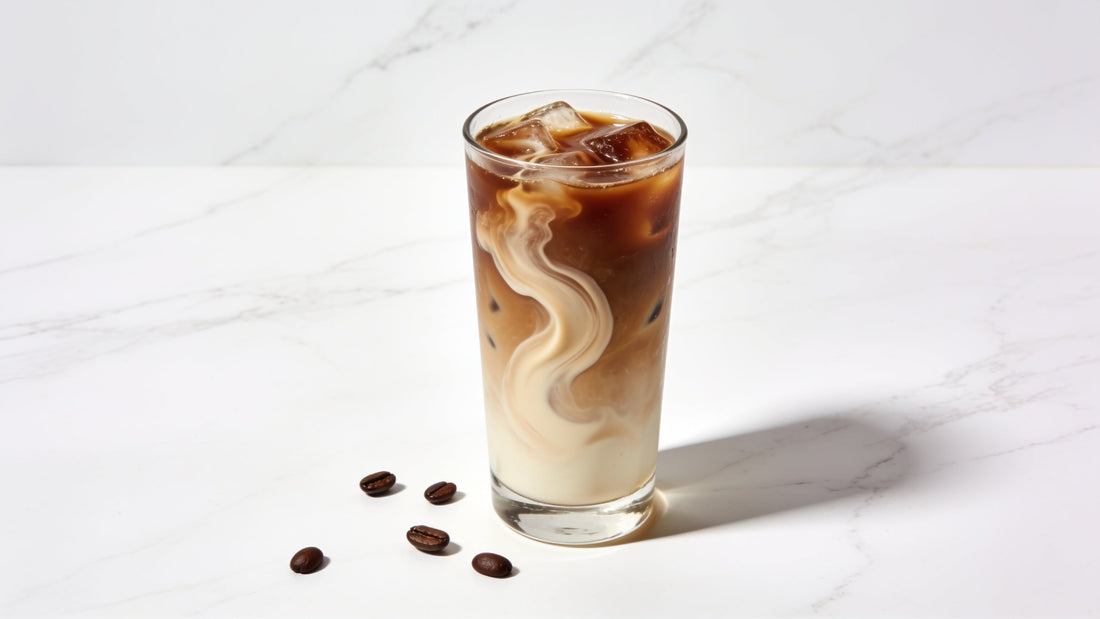 A single tall glass of iced coffee with a light cream swirl on a clean white marble surface
