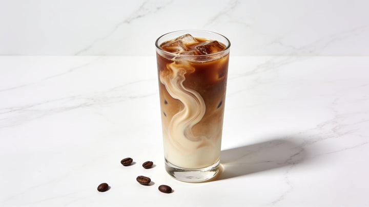 A single tall glass of iced coffee with a light cream swirl on a clean white marble surface